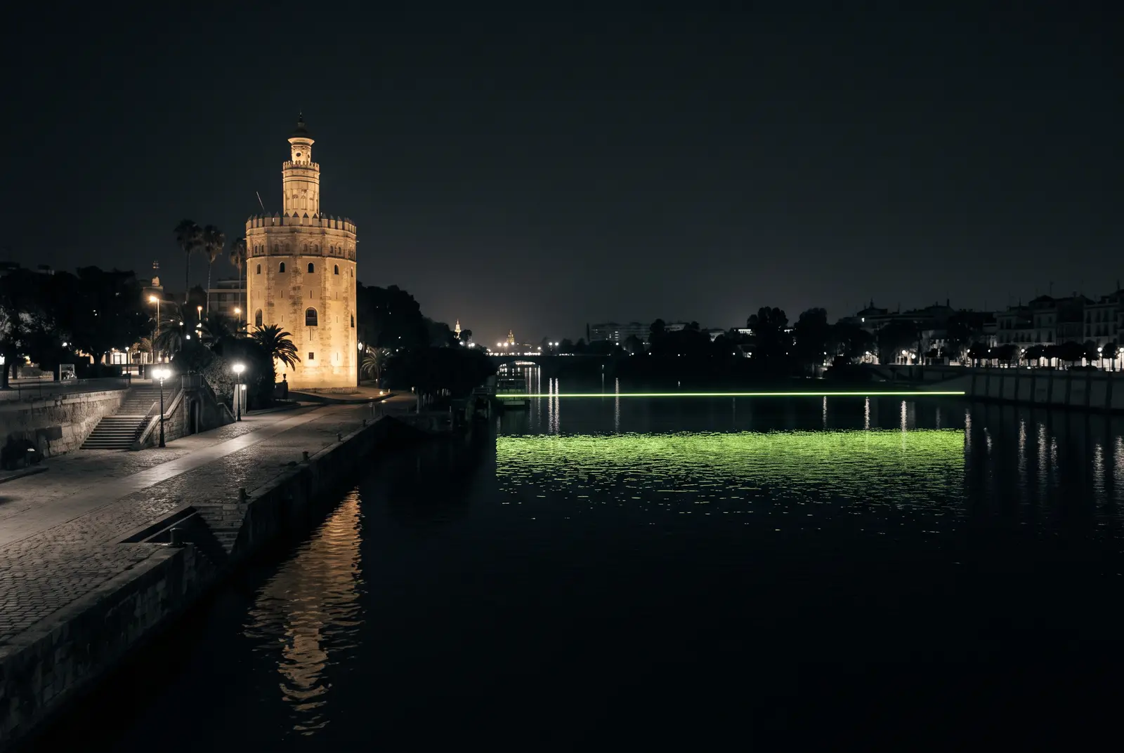 La Torre del Oro junto al Guadalquivir de noche con una linea lima en el agua